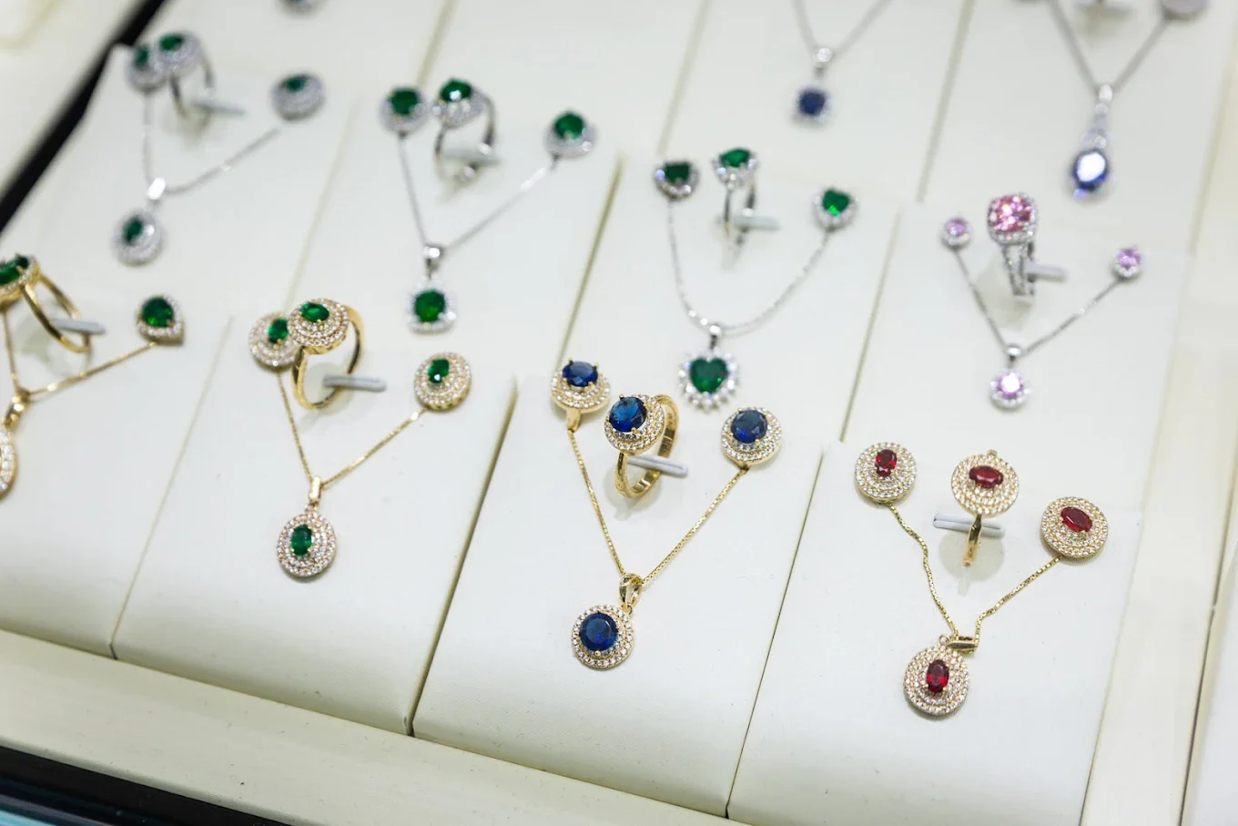 Emerald, sapphire and ruby pendant, ring and earring sets on white display stands