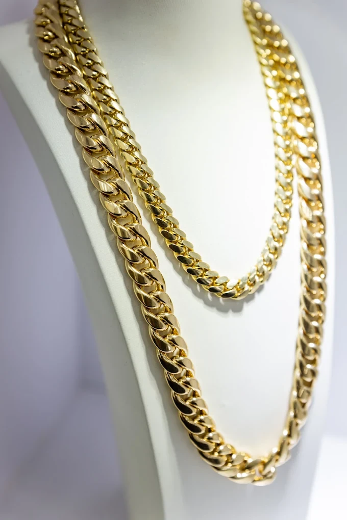 Two solid gold Miami Cuban link chains layered on a white bust