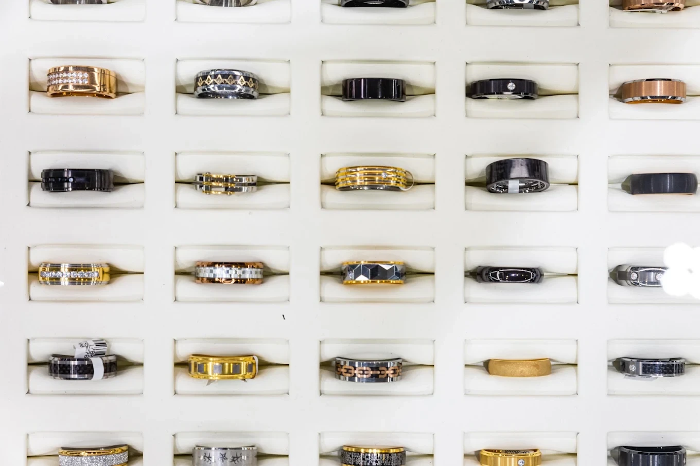 Rows of men’s bands in gold, black and two-tone finishes on a white display wall