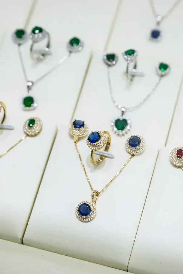 Emerald, sapphire and ruby pendant, ring and earring sets in gold and silver on white display stands